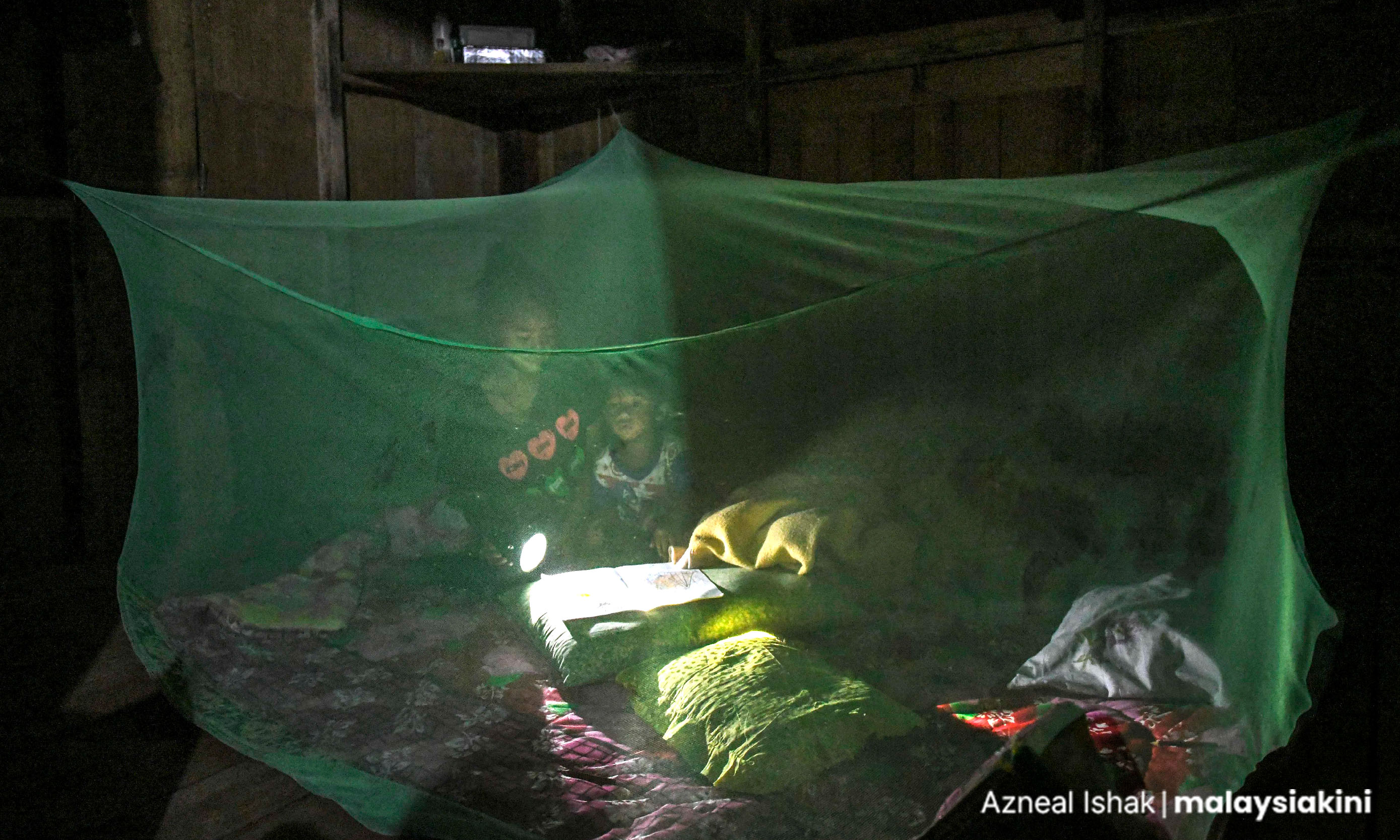 In Pos Lanai, Pahang, a mother reads her son a bedtime story using a battery-powered torchlight.